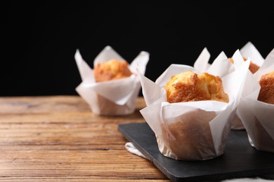 Photo of Delicious sweet muffins on wooden table against dark background, closeup. Space for text