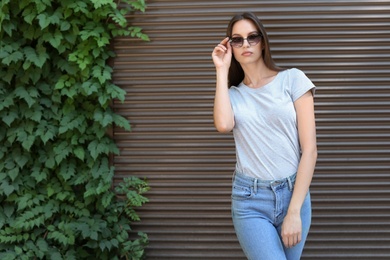 Young woman wearing gray t-shirt near wall on street. Urban style