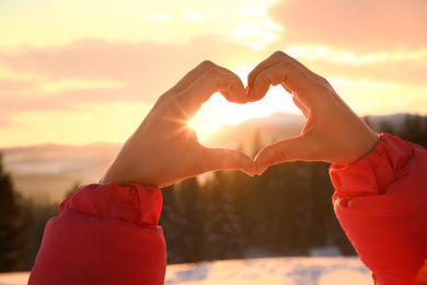 Woman making heart with hands outdoors at sunset, closeup. Winter vacation