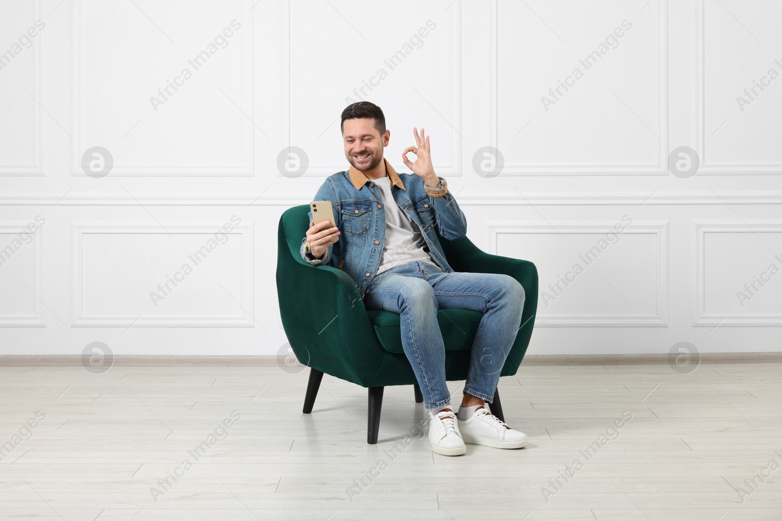 Photo of Happy man sitting in armchair and having video chat via smartphone indoors