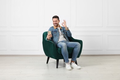 Happy man sitting in armchair and having video chat via smartphone indoors