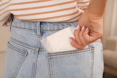 Photo of Woman putting disposable menstrual pad into pocket indoors, closeup