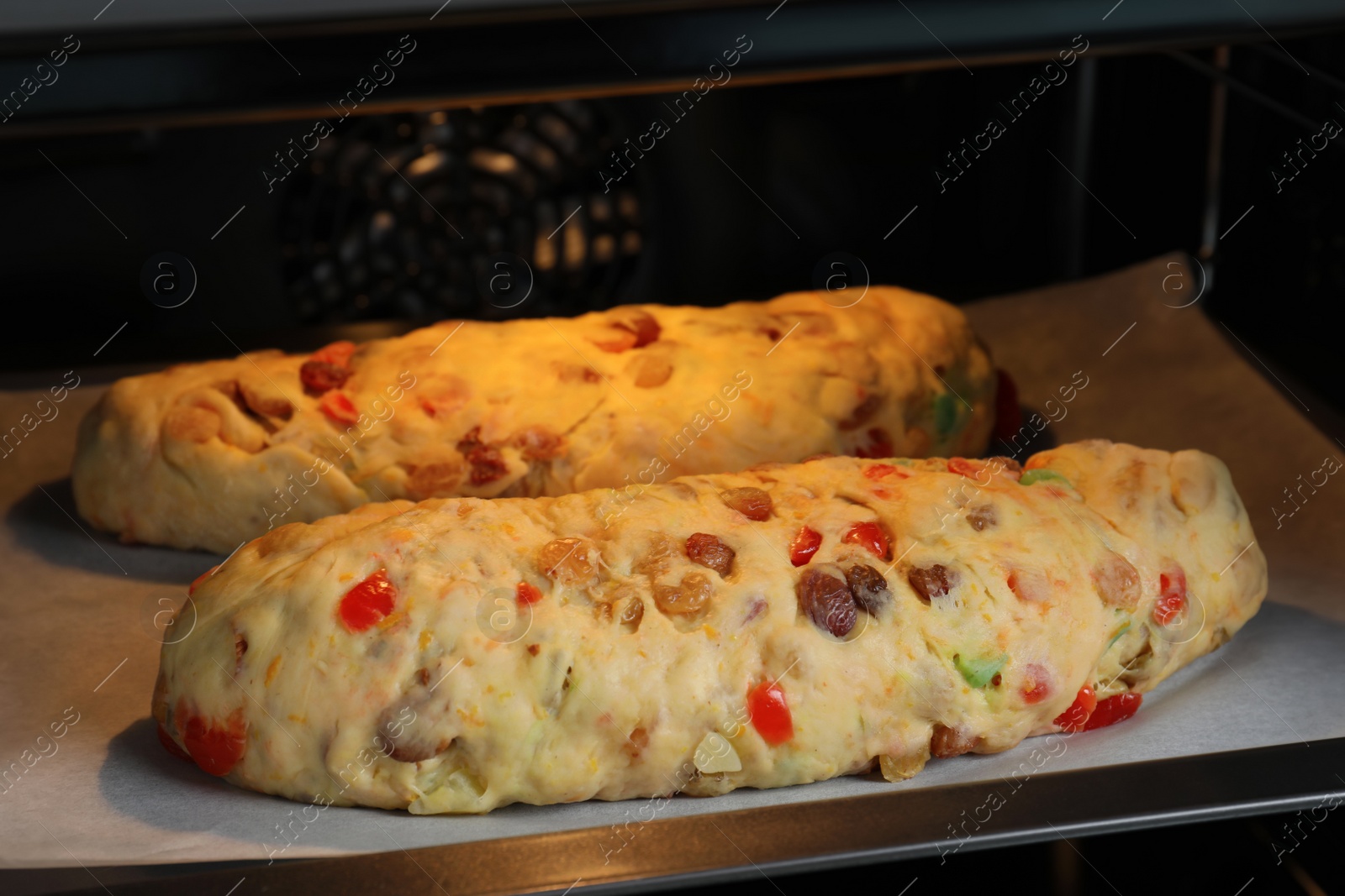Photo of Raw homemade Stollens with candied fruits and nuts on baking tray in oven, closeup. Traditional German Christmas bread