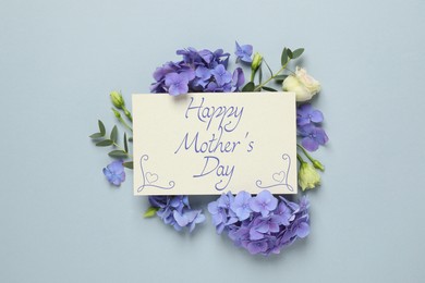 Happy Mother's Day greeting card and beautiful flowers on pale light blue background, flat lay