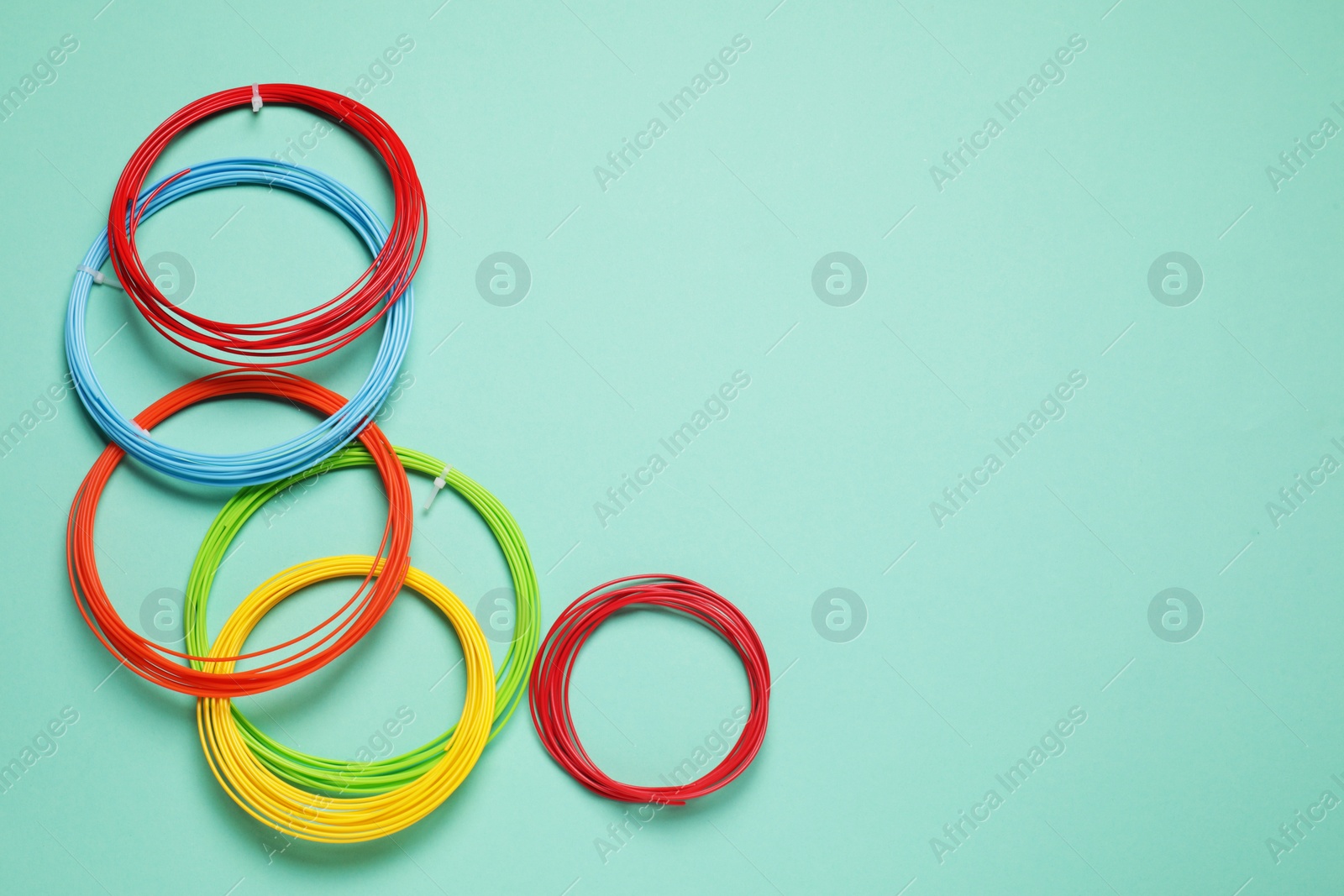 Photo of Colorful plastic filaments for 3D pen on turquoise background, flat lay. Space for text
