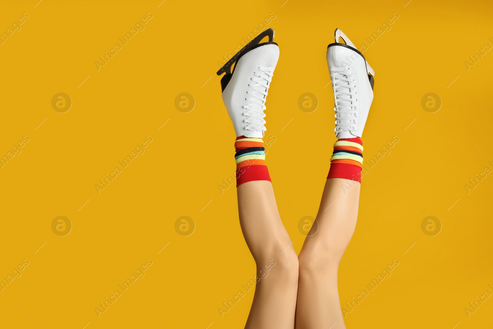 Photo of Woman in elegant white ice skates on yellow background, closeup of legs. Space for text