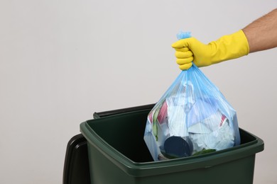 Man throwing garbage bag into bin on light background, closeup. Space for text