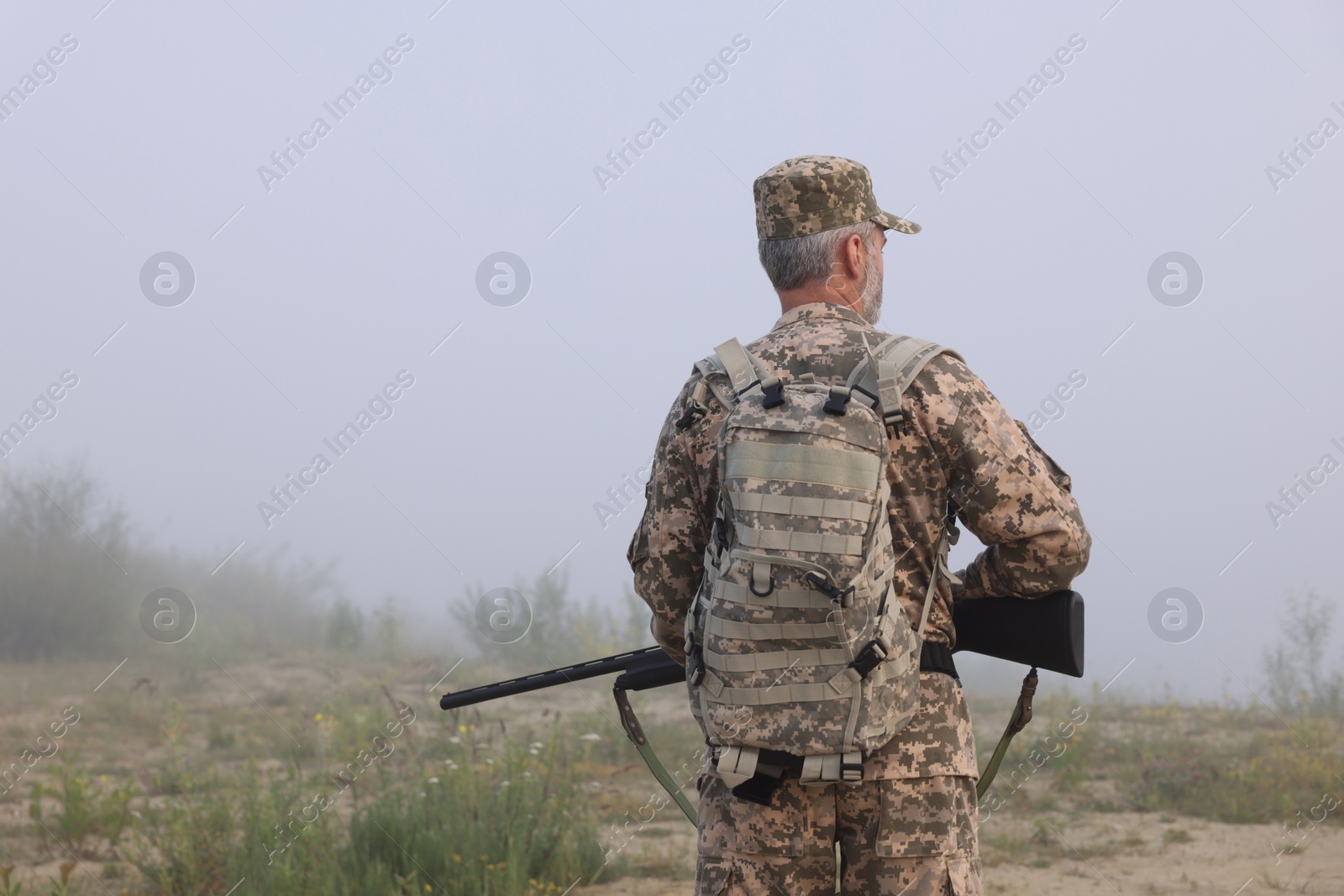 Photo of Man wearing camouflage with hunting rifle outdoors, back view. Space for text