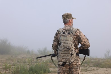 Man wearing camouflage with hunting rifle outdoors, back view. Space for text