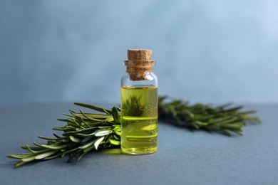 Bottle with rosemary essential oil and fresh herb on table