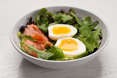 Delicious salad with boiled egg, salmon and arugula on white wooden table, closeup