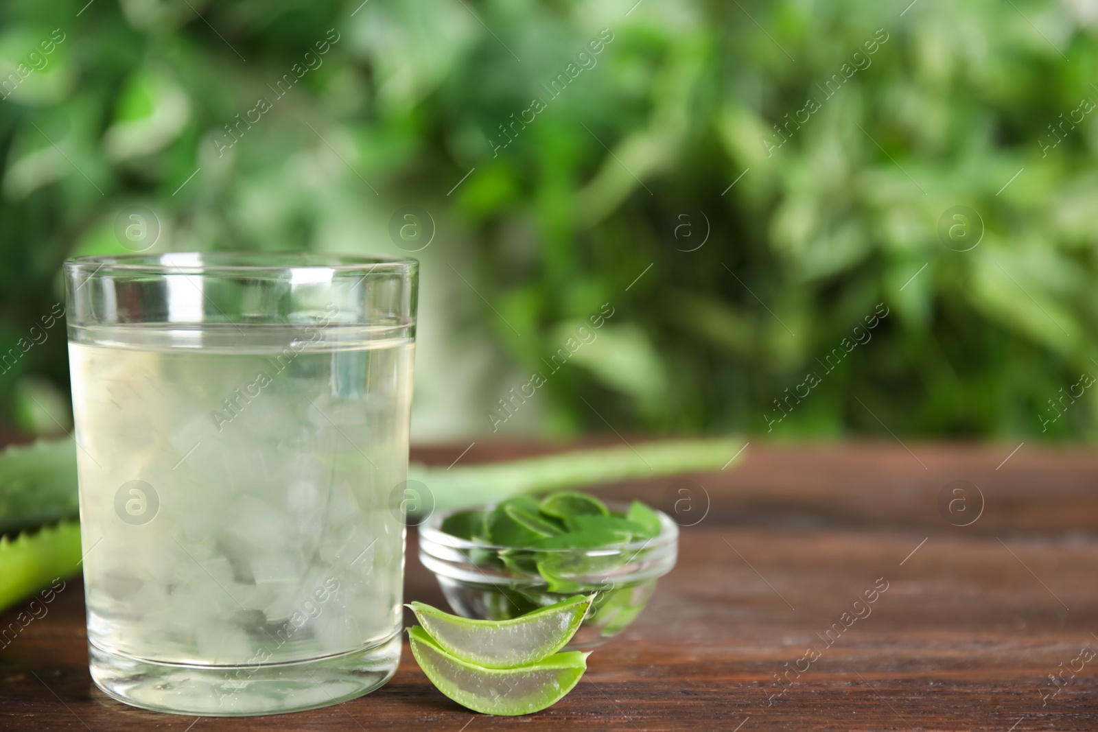 Photo of Fresh aloe drink in glass and leaves on wooden table, space for text