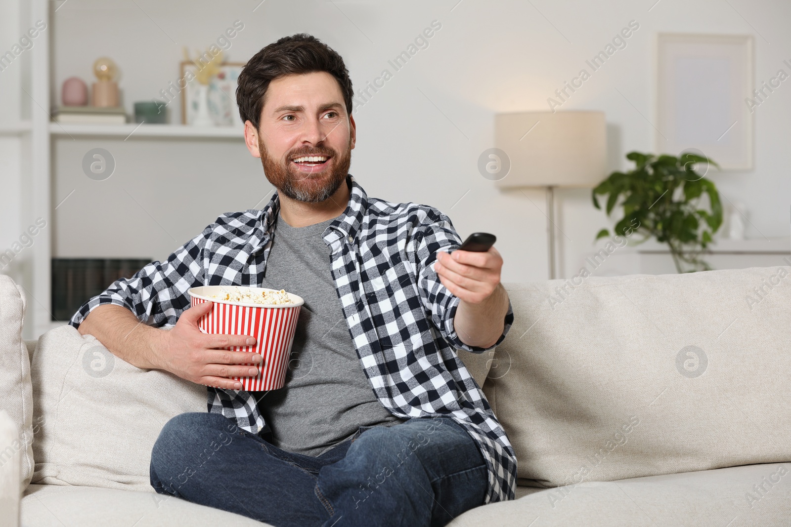 Photo of Happy man watching TV with popcorn on sofa indoors