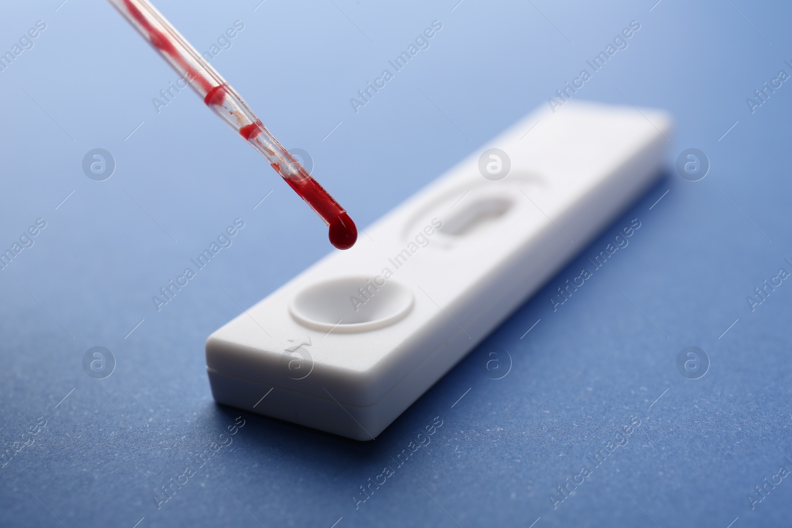 Photo of Dropping blood sample onto disposable express test cassette with pipette on blue background, closeup