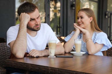 Photo of Young man having boring date with talkative girl in outdoor cafe