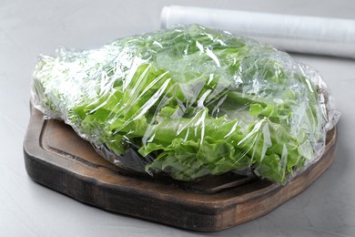 Photo of Fresh lettuce with plastic food wrap on light grey table, closeup