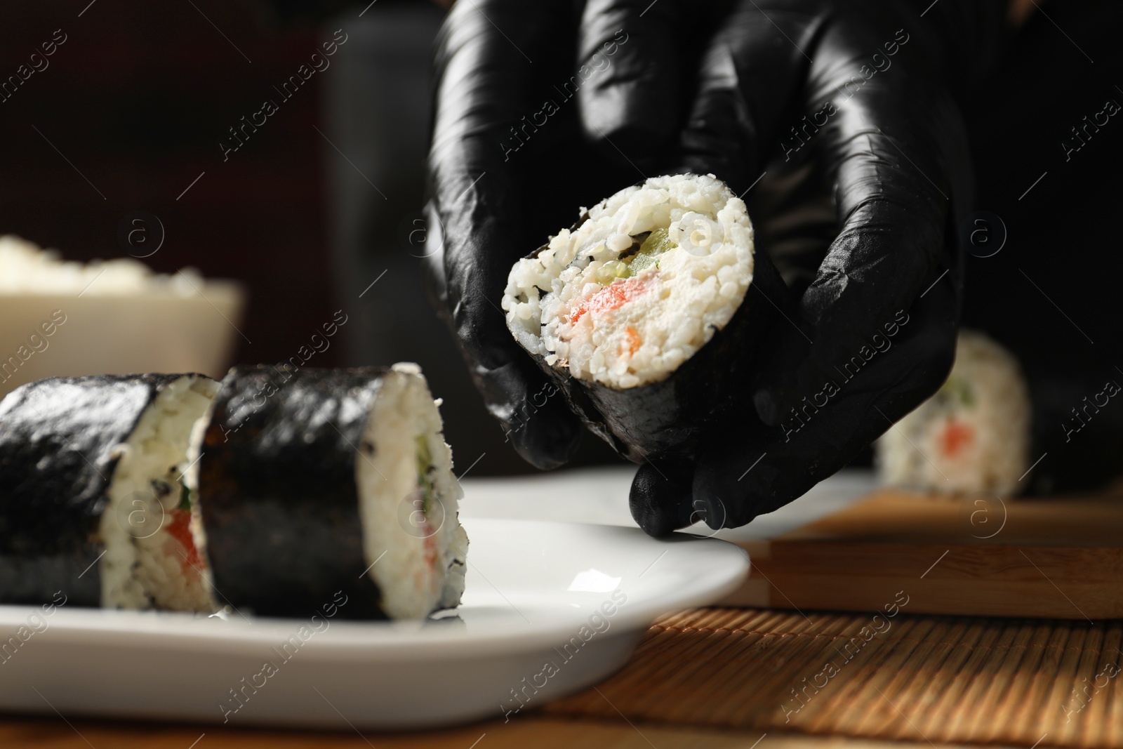 Photo of Chef in gloves putting sushi roll onto dish at table, closeup