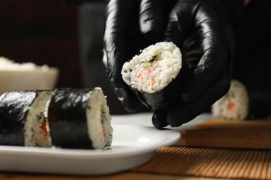 Photo of Chef in gloves putting sushi roll onto dish at table, closeup