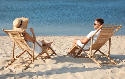 Photo of Young couple relaxing in deck chairs on beach