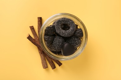 Photo of Jar with tasty candies and dried liquorice roots on yellow background, top view