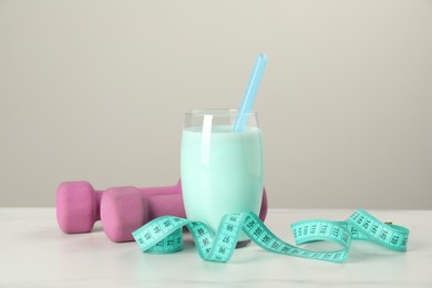 Photo of Tasty shake, dumbbells and measuring tape on white table. Weight loss