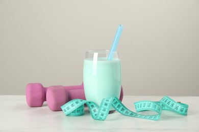 Tasty shake, dumbbells and measuring tape on white table. Weight loss