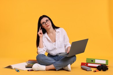 Student with laptop sitting among books and stationery on yellow background