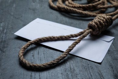 Rope noose and blank envelope on black table, closeup