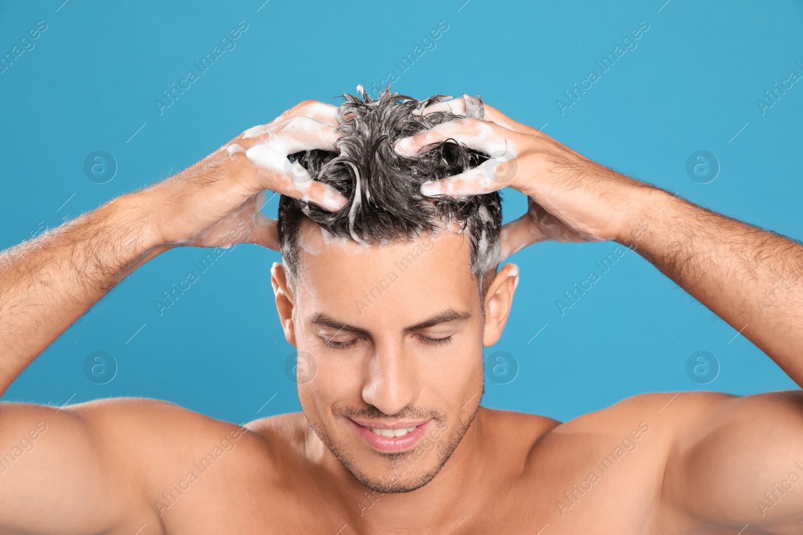 Photo of Handsome man washing hair on light blue background