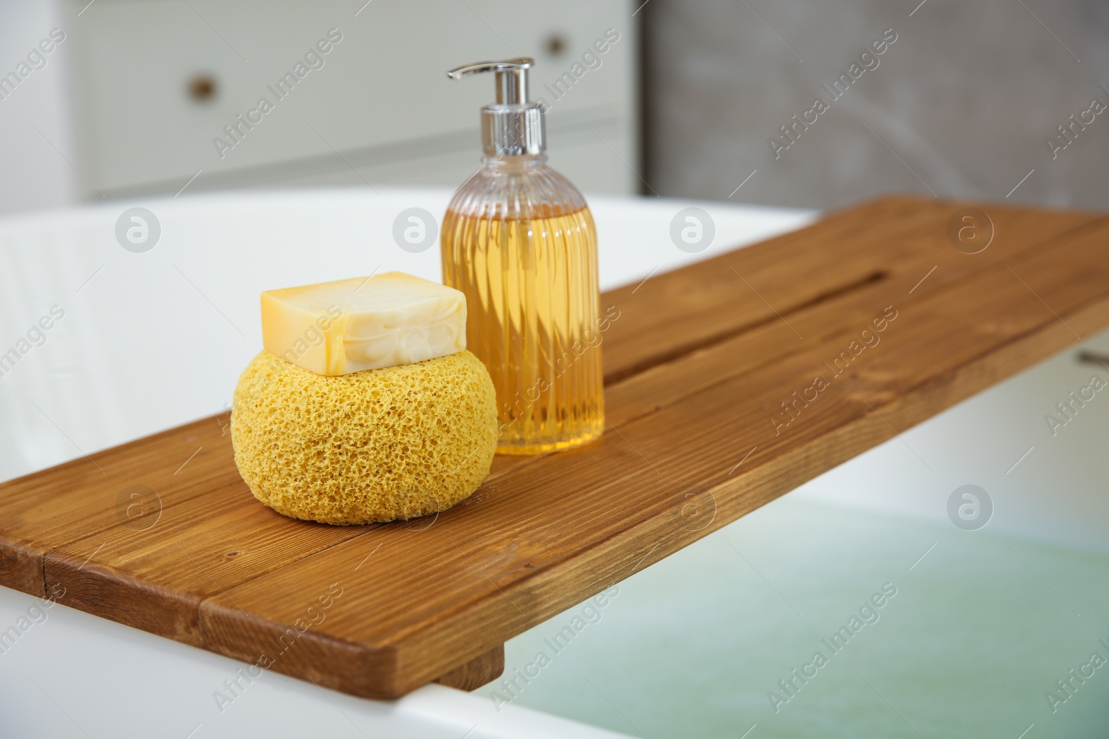 Photo of Wooden bath tray with sponge, soap bar and dispenser on tub