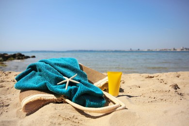 Photo of Sunscreen, starfish, bag and towel on beach, space for text. Sun protection care