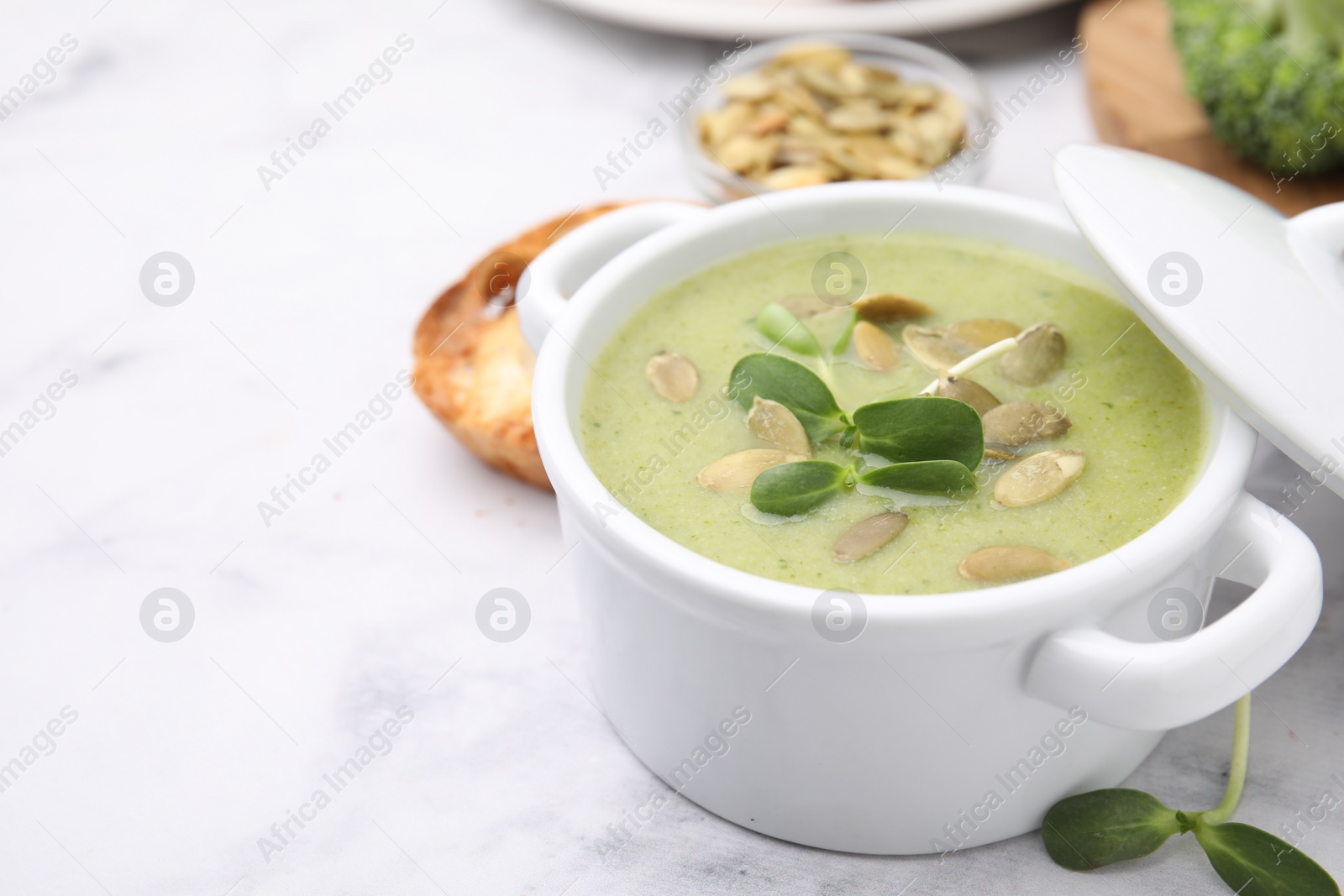 Photo of Delicious broccoli cream soup with pumpkin seeds on white marble table, space for text