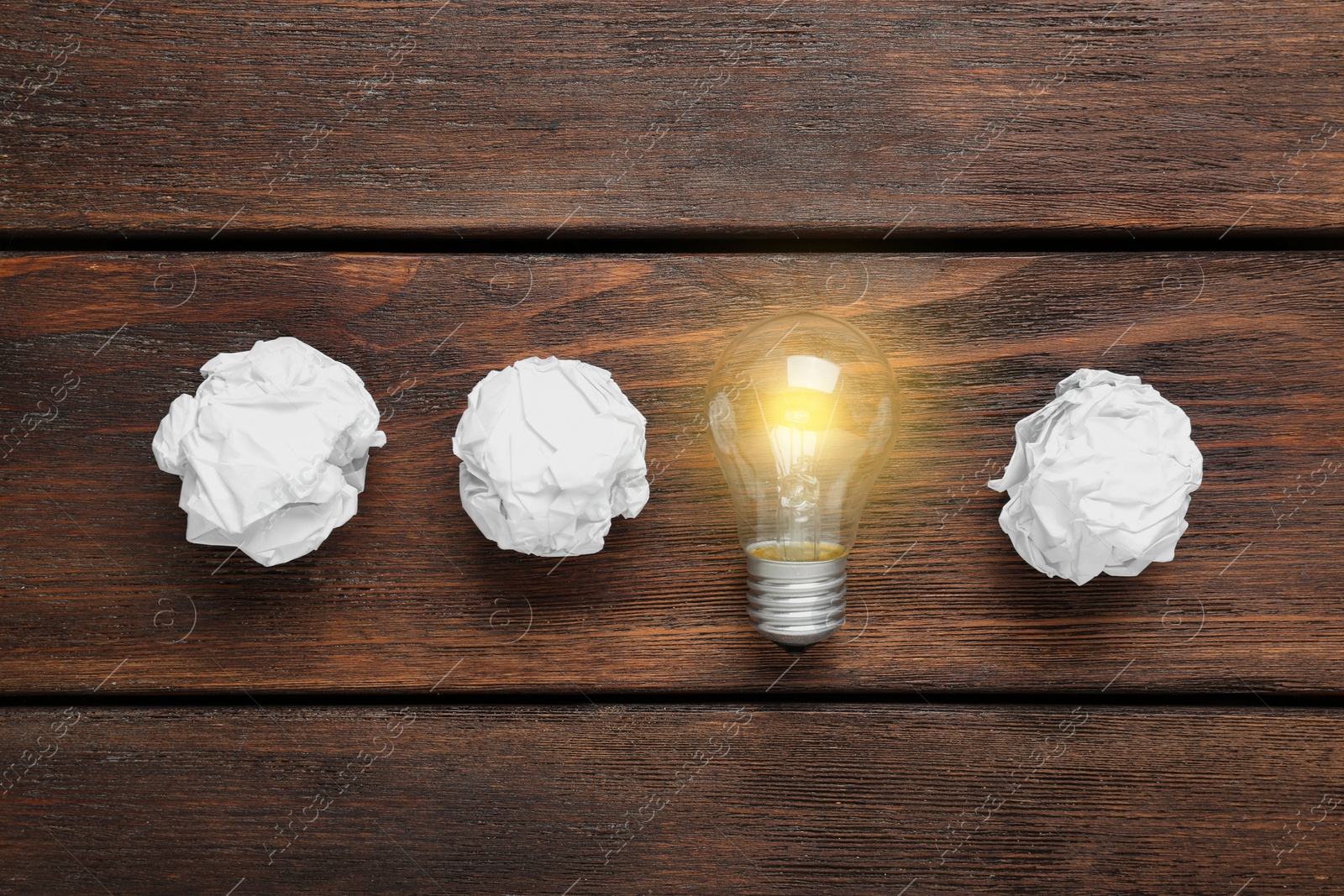 Photo of Crumpled paper balls and lamp bulb on wooden table, flat lay. Idea concept