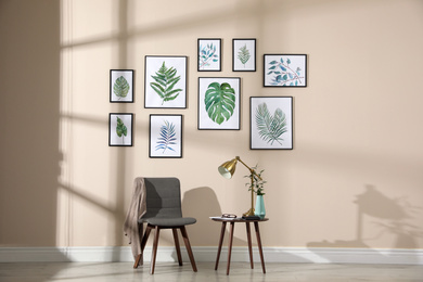 Photo of Beautiful paintings of tropical leaves on beige wall in room interior