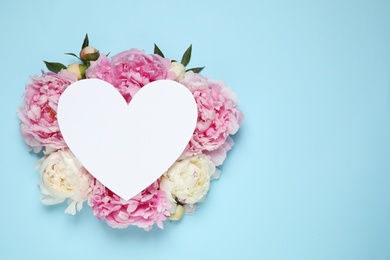 Beautiful peonies and blank heart shaped card on light blue background, flat lay. Space for text