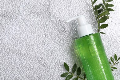 Photo of Bottle of face cleansing product and green leaves on white textured table, flat lay. Space for text