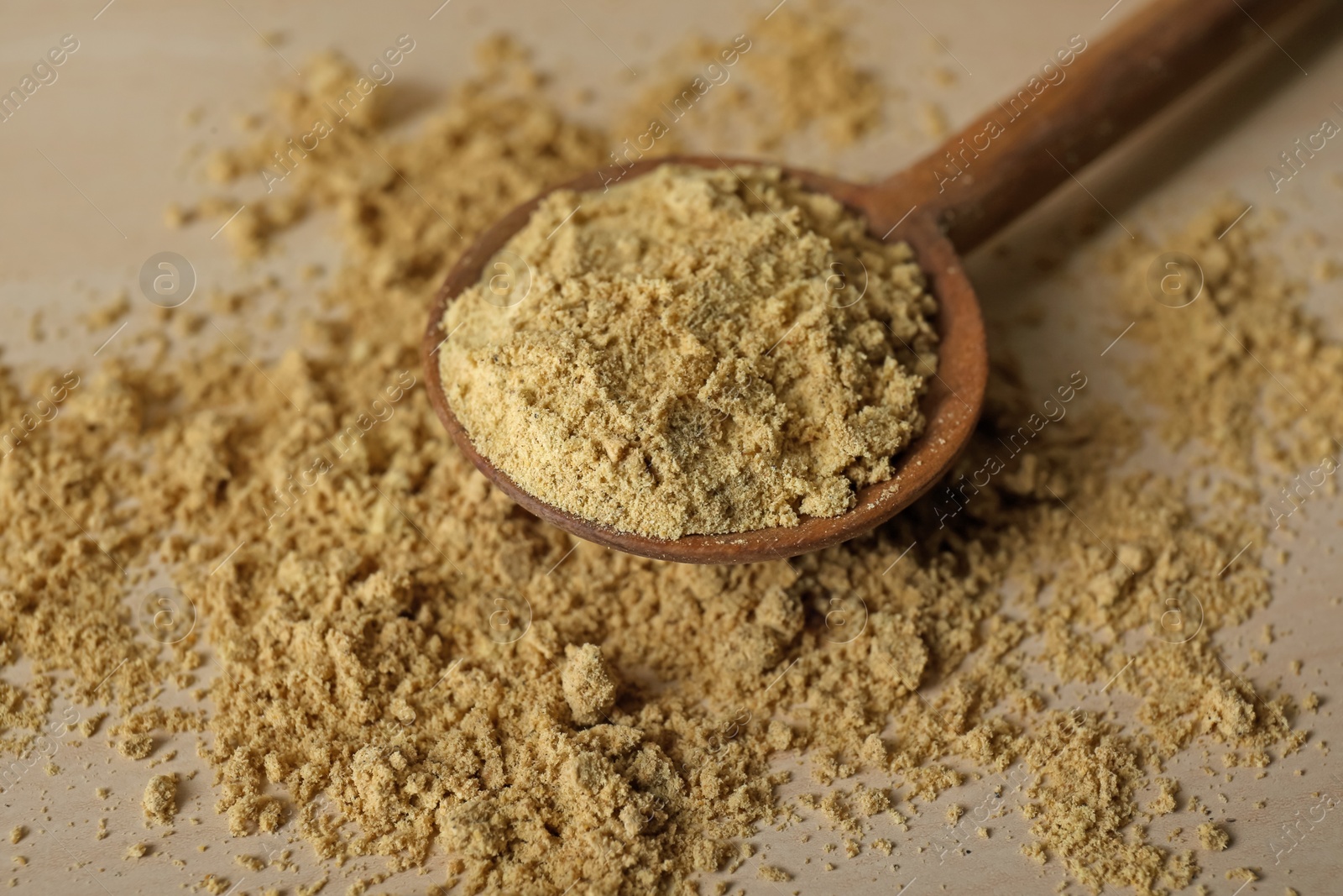 Photo of Spoon with aromatic mustard powder on wooden table, closeup