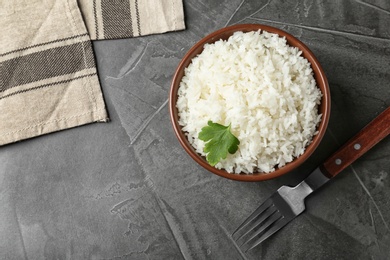 Photo of Bowl of boiled rice served on grey table, top view with space for text