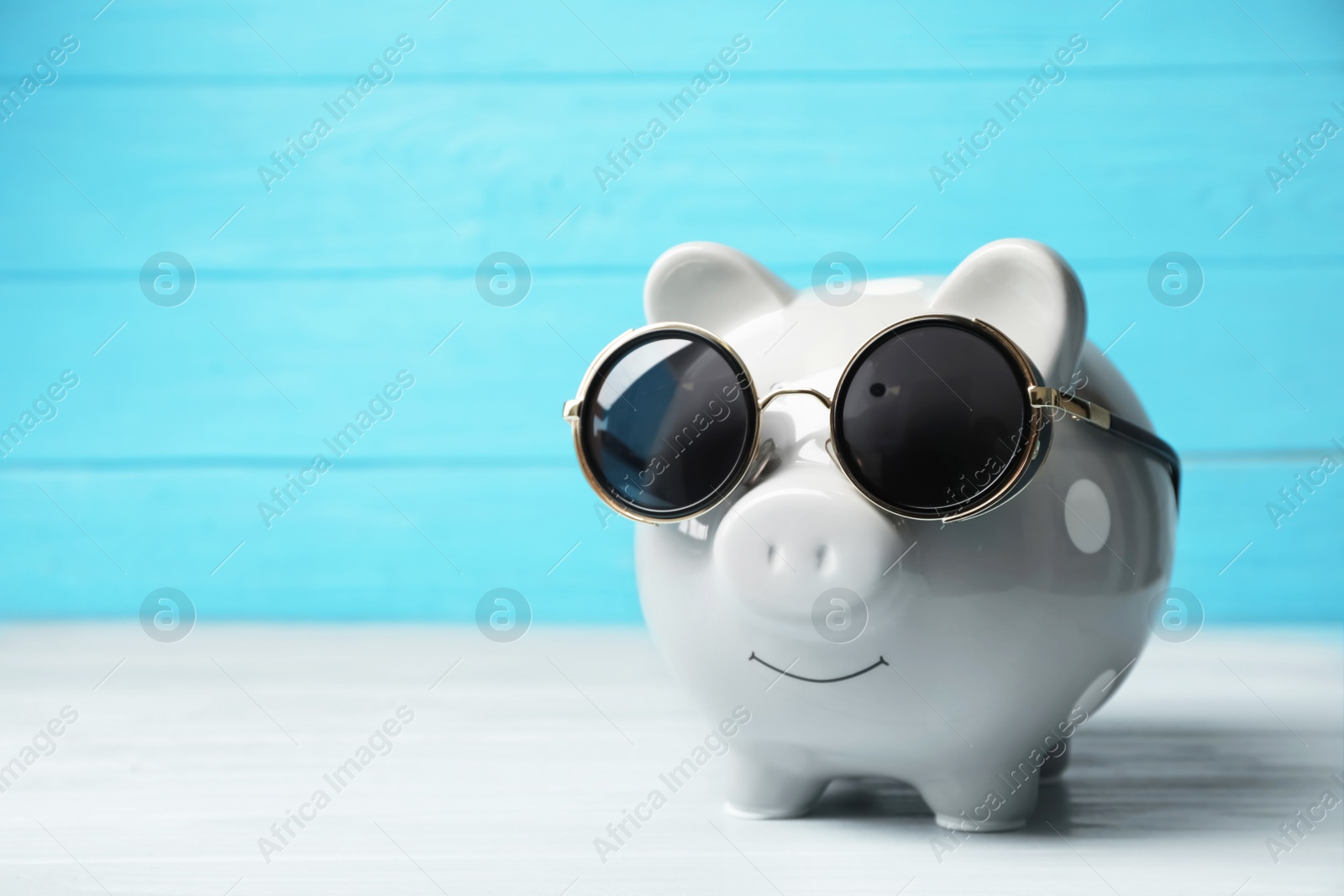 Photo of Piggy bank with sunglasses on table. Space for text