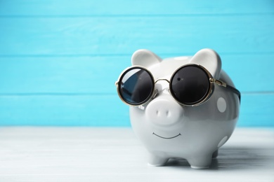 Photo of Piggy bank with sunglasses on table. Space for text