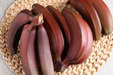 Photo of Delicious red baby bananas on wicker mat, top view