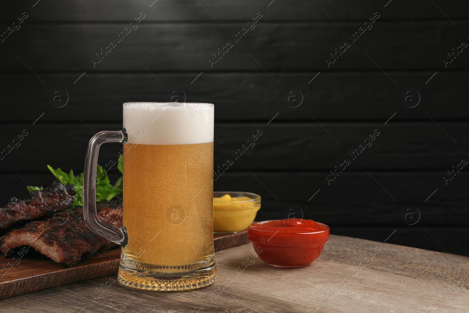 Photo of Mug with beer, delicious grilled ribs and sauces on wooden table. Space for text