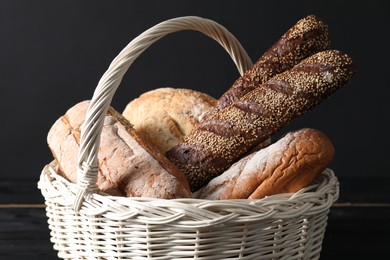 Photo of Wicker basket with different types of fresh bread on black table