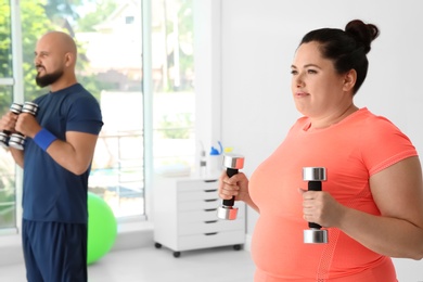 Overweight man and woman doing exercise with dumbbells in gym