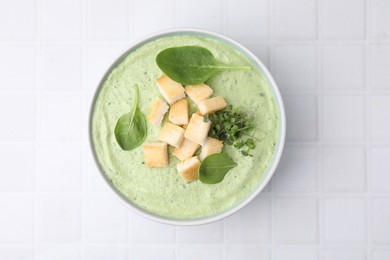 Photo of Delicious spinach cream soup with croutons in bowl on white tiled table, top view