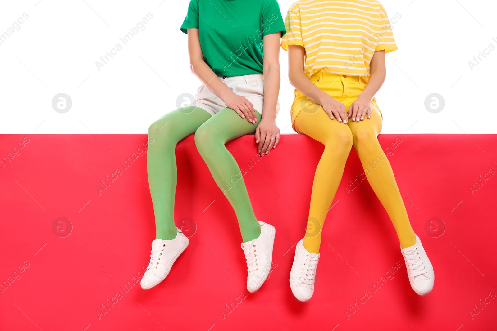 Photo of Women wearing bright tights sitting together on color background, closeup