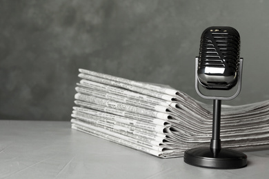 Photo of Newspapers and vintage microphone on light grey stone table. Journalist's work