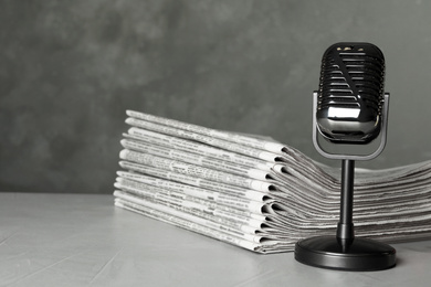 Newspapers and vintage microphone on light grey stone table. Journalist's work