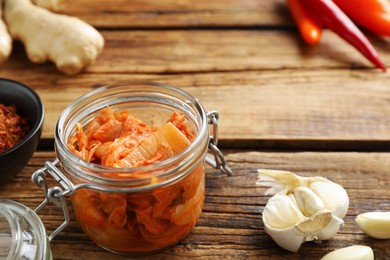 Photo of Glass jar of delicious kimchi with Chinese cabbage and ingredients on wooden table