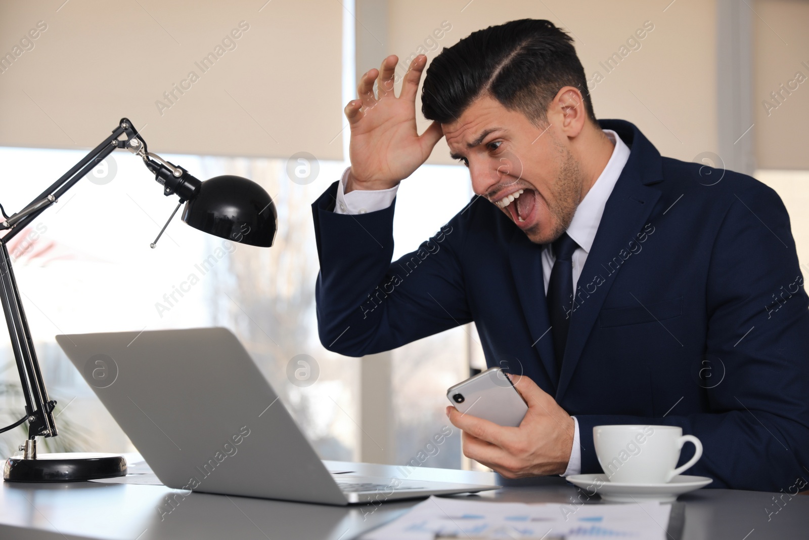 Photo of Emotional businessman with laptop and smartphone at table in office